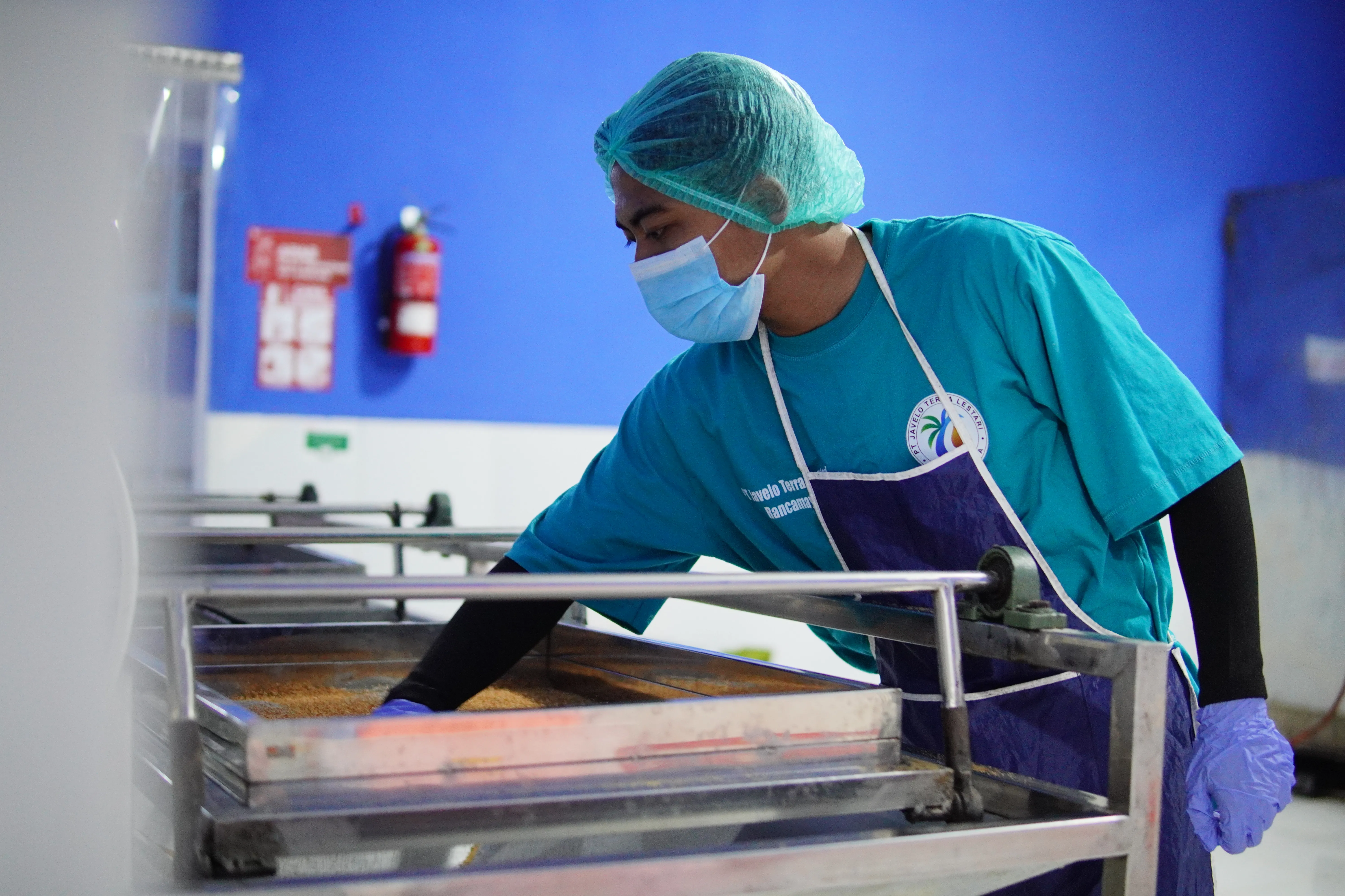 Javelo worker in a hairnet, mask and gloves checking production data on a tablet